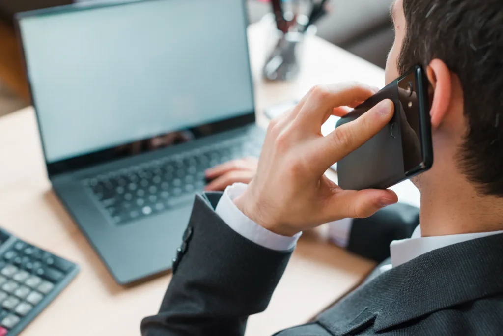 Businessman talking on smartphone beside open laptop