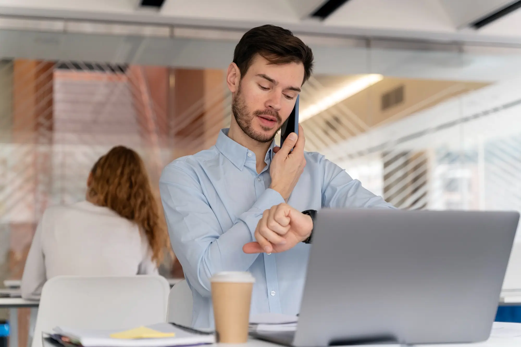 Man talking on phone while checking time at laptop