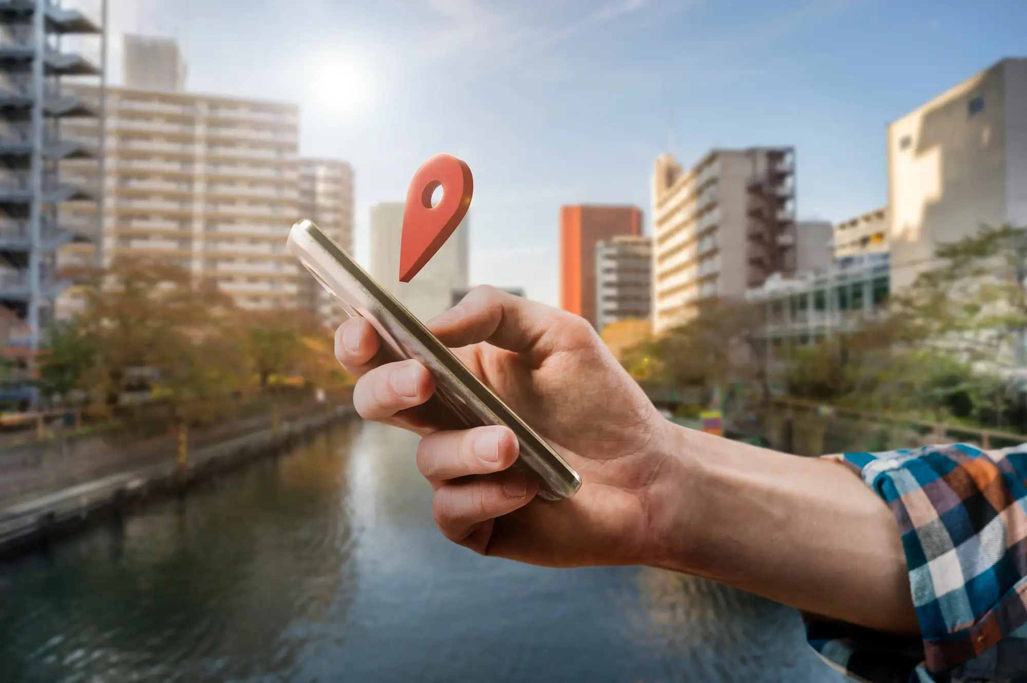 Hand holding smartphone with location pin over city canal